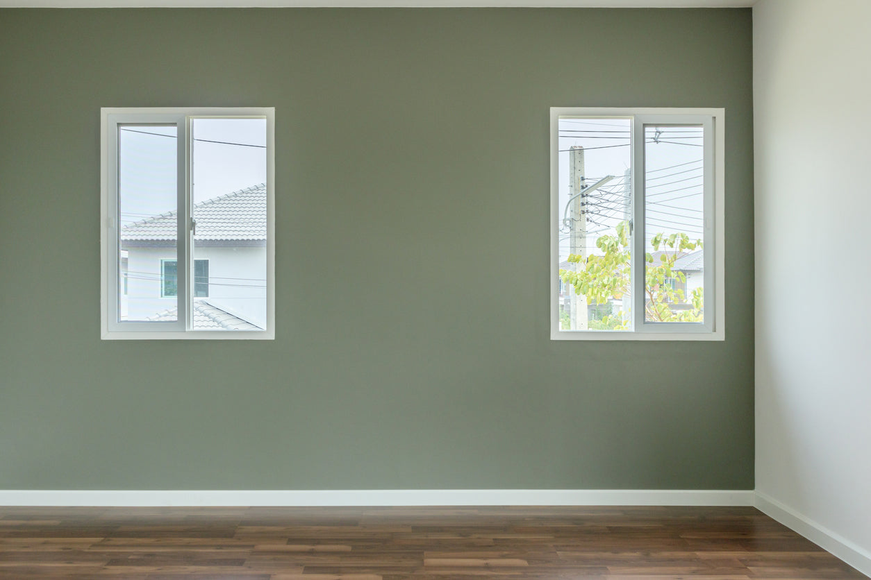 Mur d'accent peint en vert sauge avec finitions blanches, deux fenêtres apportant une lumière naturelle et parquet en bois foncé dans une pièce rénovée par La Haute Peinture en Haute-Savoie.