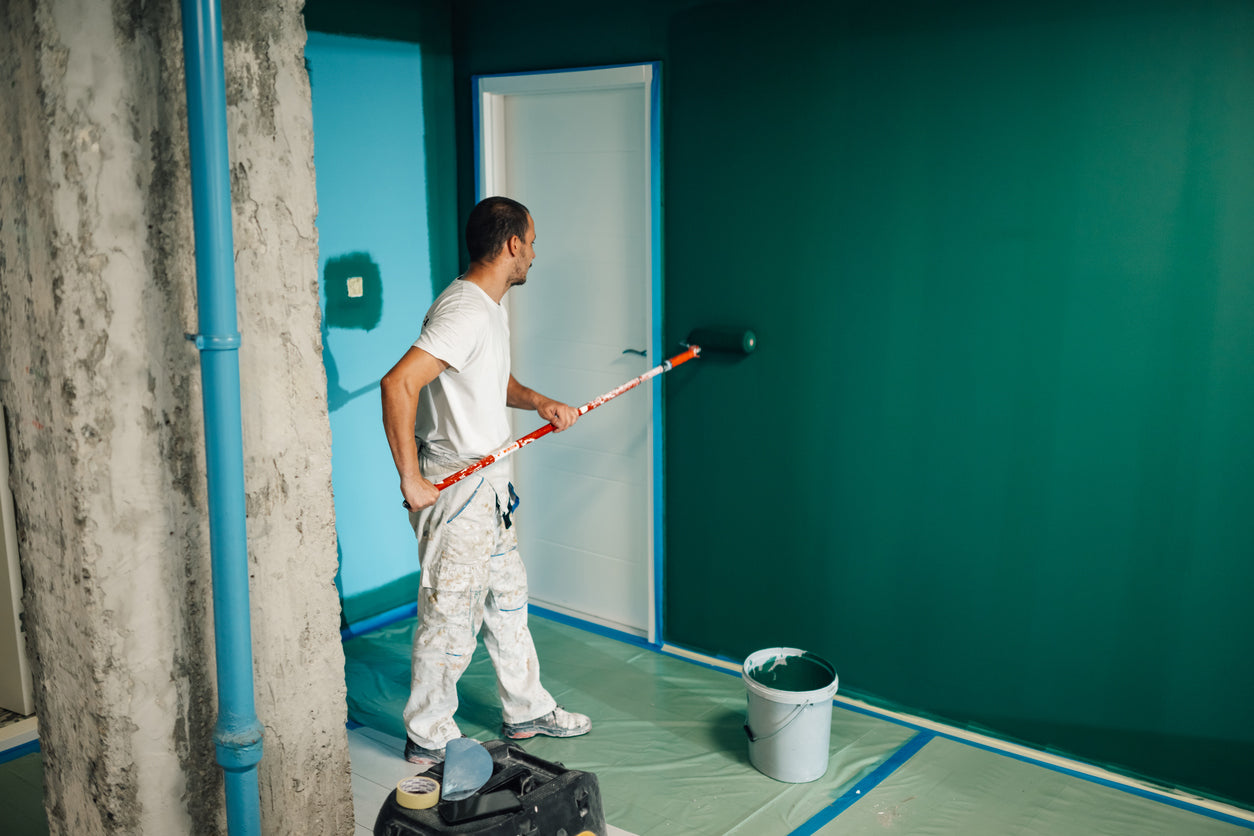 Artisan peintre appliquant une peinture murale verte au rouleau dans une pièce en rénovation en Haute-Savoie, avec protection du sol et finitions soignées réalisées par La Haute Peinture.