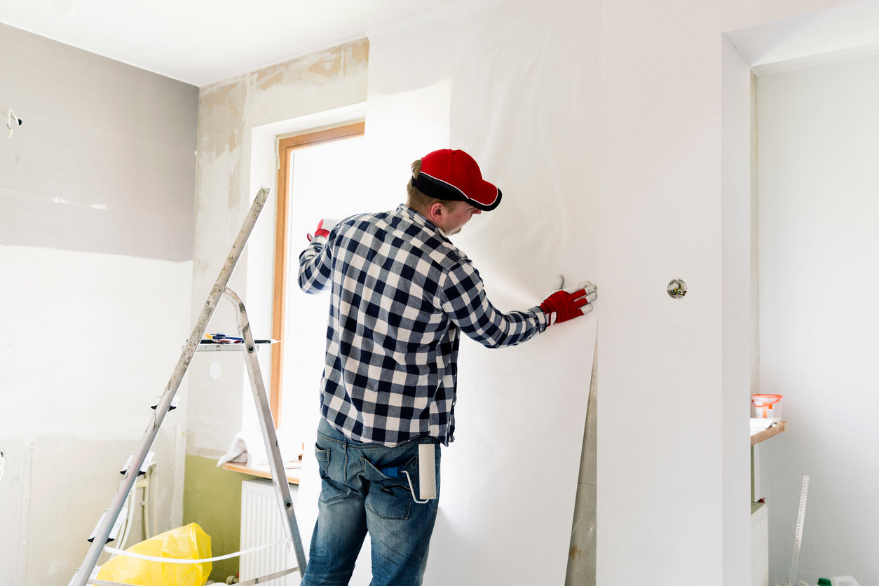 Artisan en train de poser un papier peint sur un mur préparé lors d'une rénovation intérieure, avec finitions soignées autour de la fenêtre, réalisées par La Haute Peinture en Haute-Savoie.