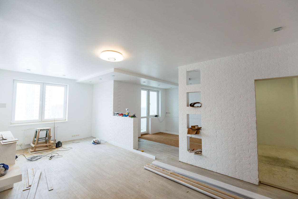 Grande pièce de vie en cours de rénovation avec murs et plafond peints en blanc, revêtement de sol en cours de pose et cloison décorative texturée, réalisée par La Haute Peinture en Haute-Savoie.
