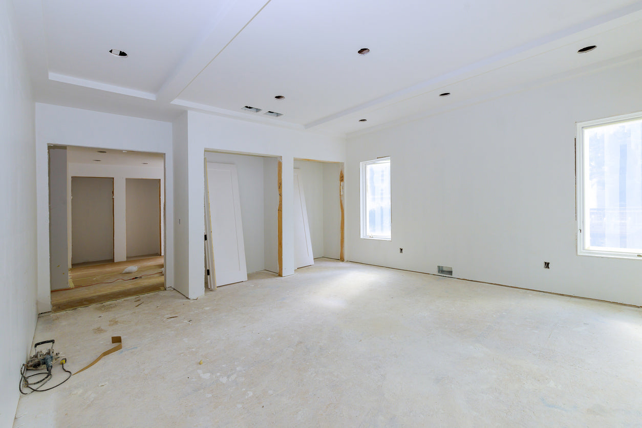 Pièce en cours de rénovation avec murs et plafond fraîchement peints en blanc, faux plafond avec spots encastrés et préparation avant la pose du revêtement de sol, réalisée par La Haute Peinture en Haute-Savoie.
